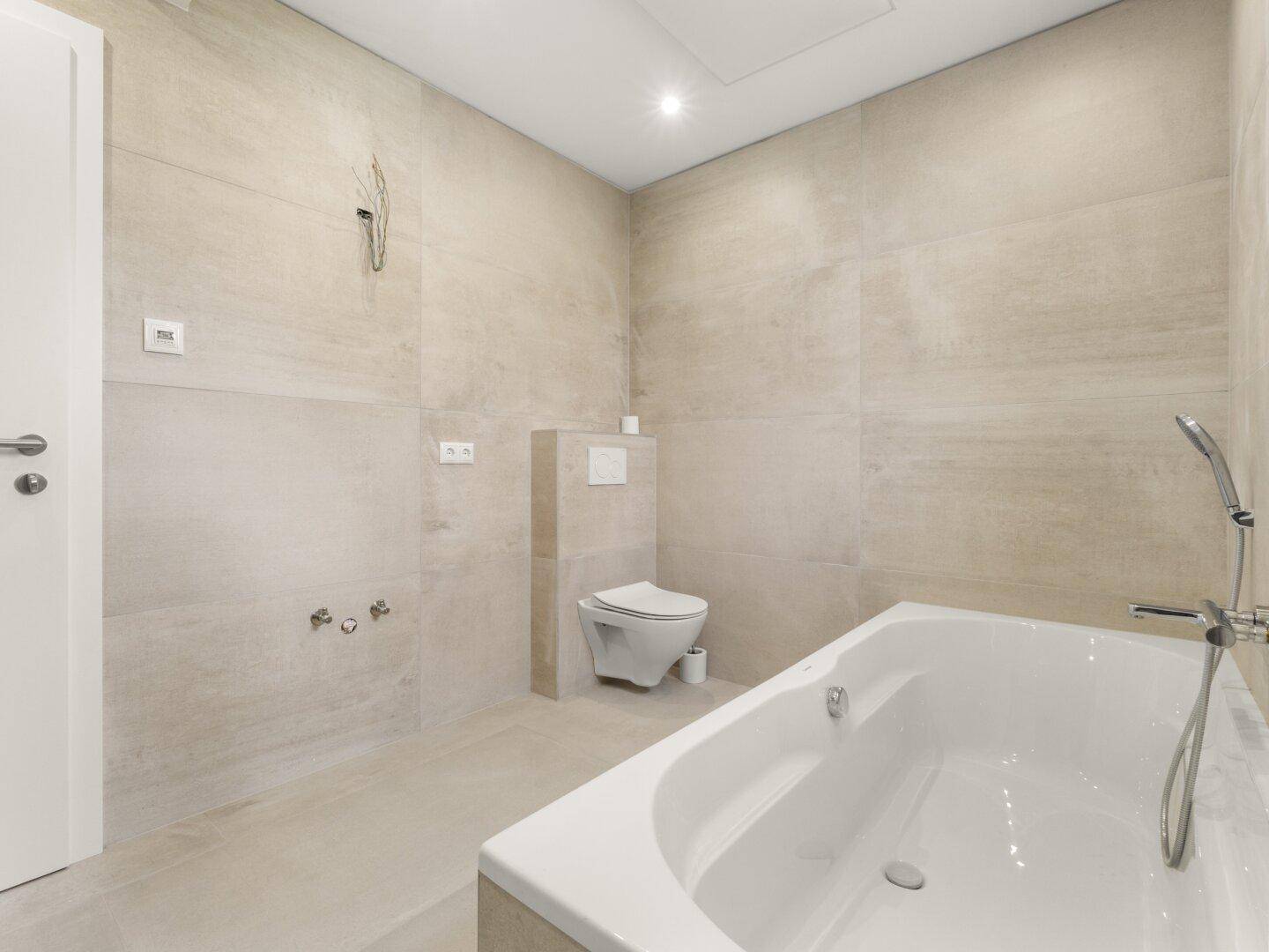 Geräumiges Badezimmer mit beigefarbenen Fliesen, Badewanne und Duschbereich.