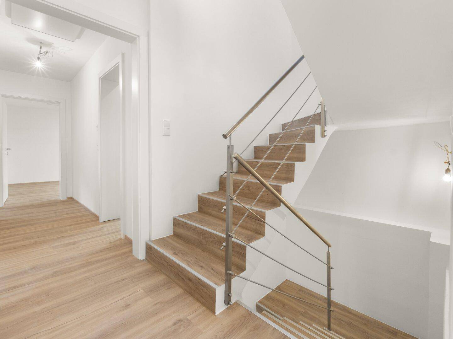Moderne Treppe mit Holzstufen und elegantem Metallgeländer, die die Etagen verbindet.