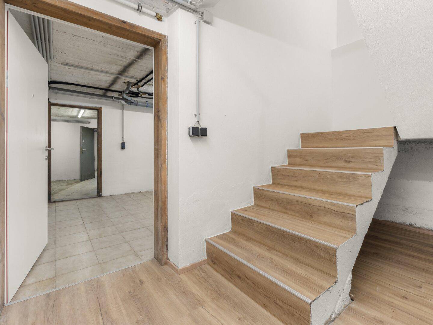 Kellerbereich mit Treppenzugang, Fliesenboden und sichtbaren Installationen, bietet Stauraum.