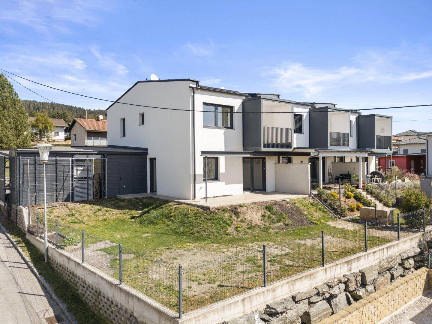 Moderne Reihenhäuser mit weißer Fassade und dunklen Akzenten, umgeben von einem kleinen Gartenbereich.