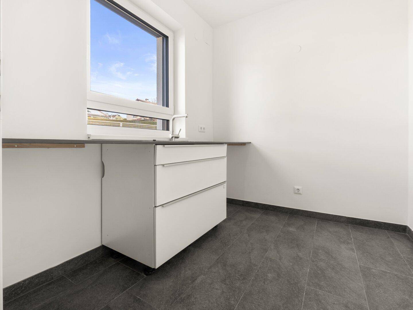 Funktionaler Hauswirtschaftsraum mit Waschbecken, Arbeitsplatte und Fenster.