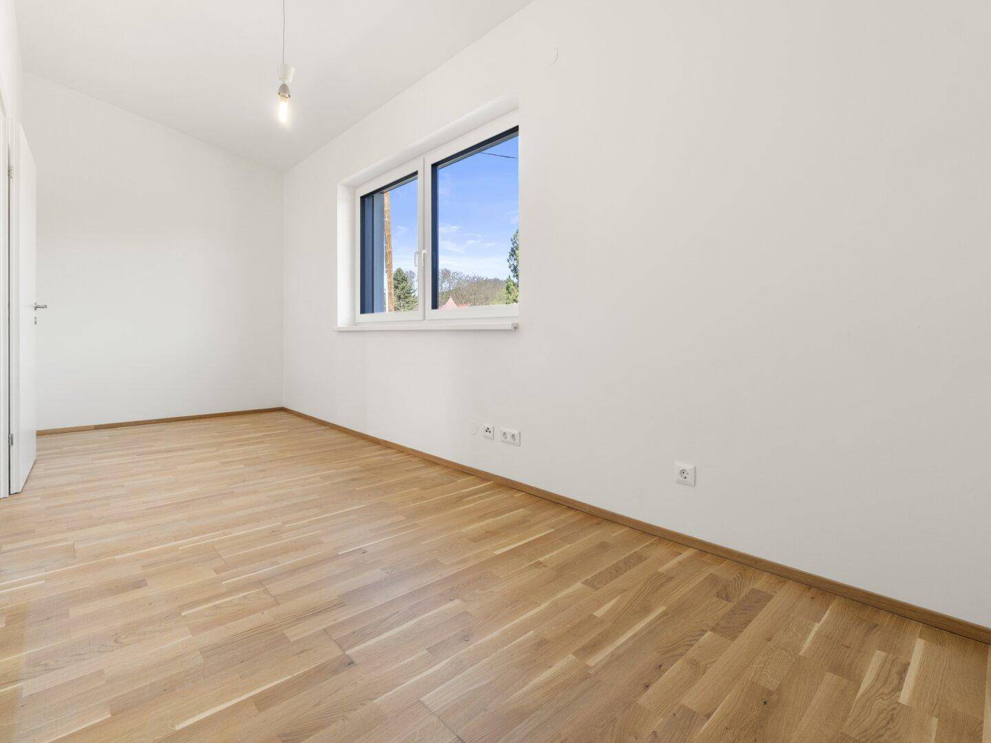 Helles, leeres Zimmer mit weiß gestrichenen Wänden und hochwertigem Parkettboden.