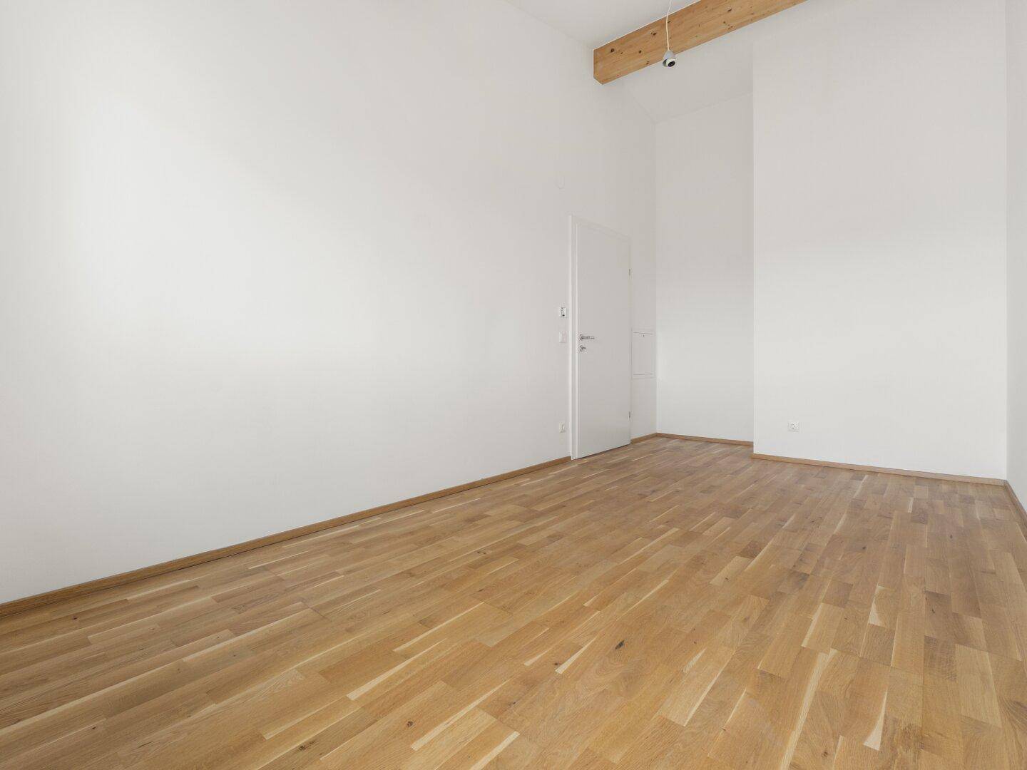 Geräumiges Zimmer mit Holzbalken an der Decke, weißen Wänden und Parkettboden.