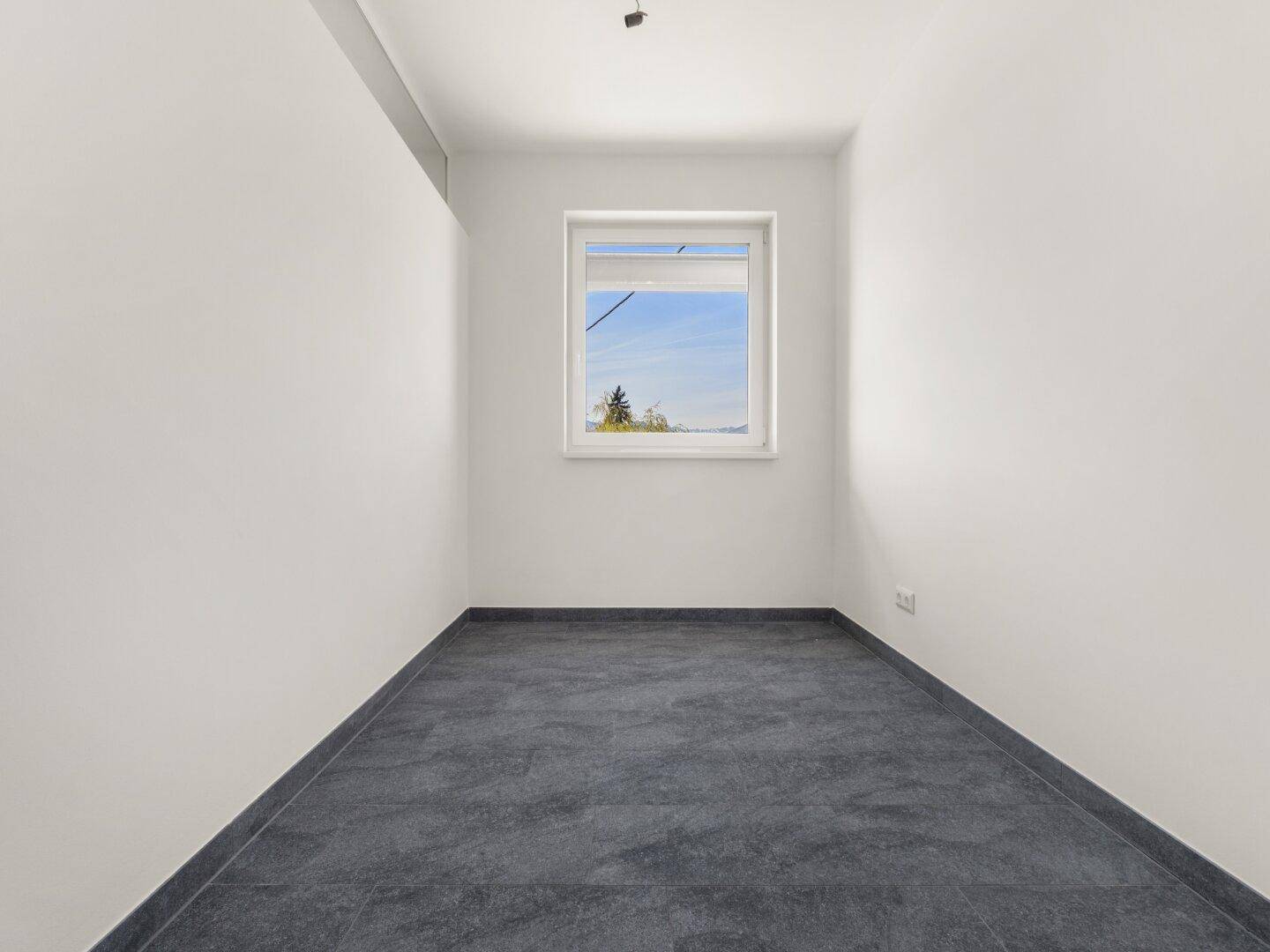 Kleiner, heller Raum mit einem Fenster und Fliesenboden, ideal als Büro oder Gästezimmer.