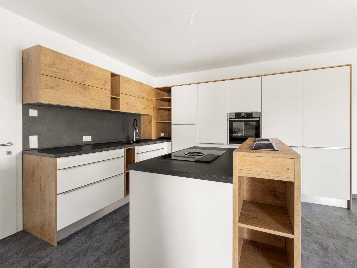 Moderne Küche mit Holz- und weißen Fronten, dunkler Arbeitsplatte und einer Kochinsel mit Induktionskochfeld.
