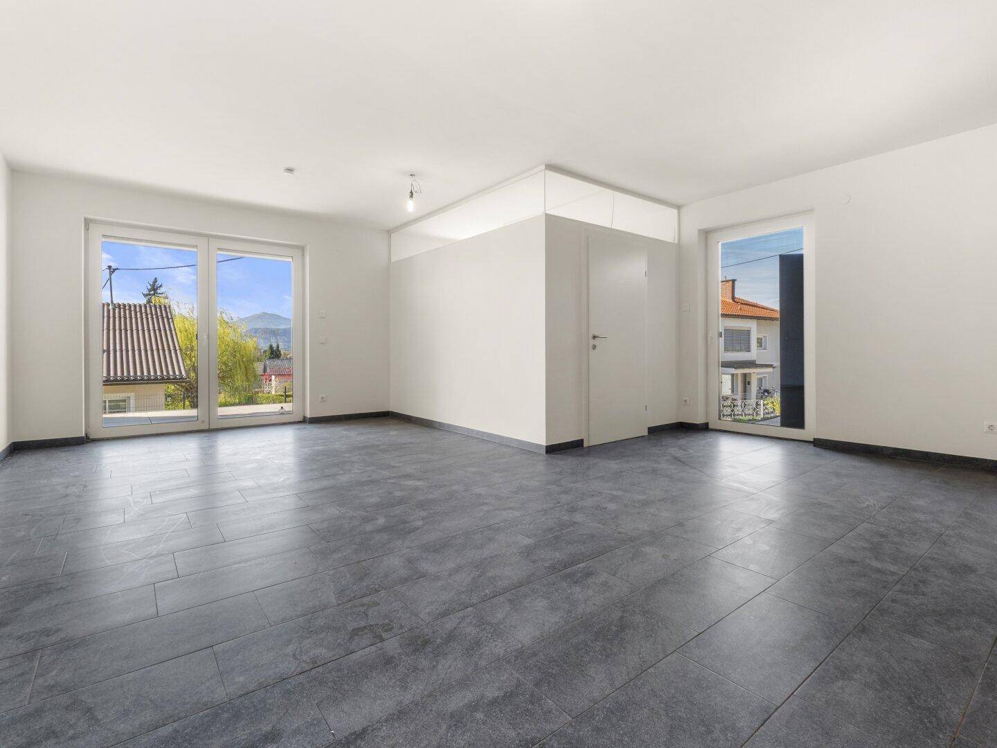 Heller, unmöblierter Wohnraum mit großen Fenstern und Zugang zu einem Außenbereich.
