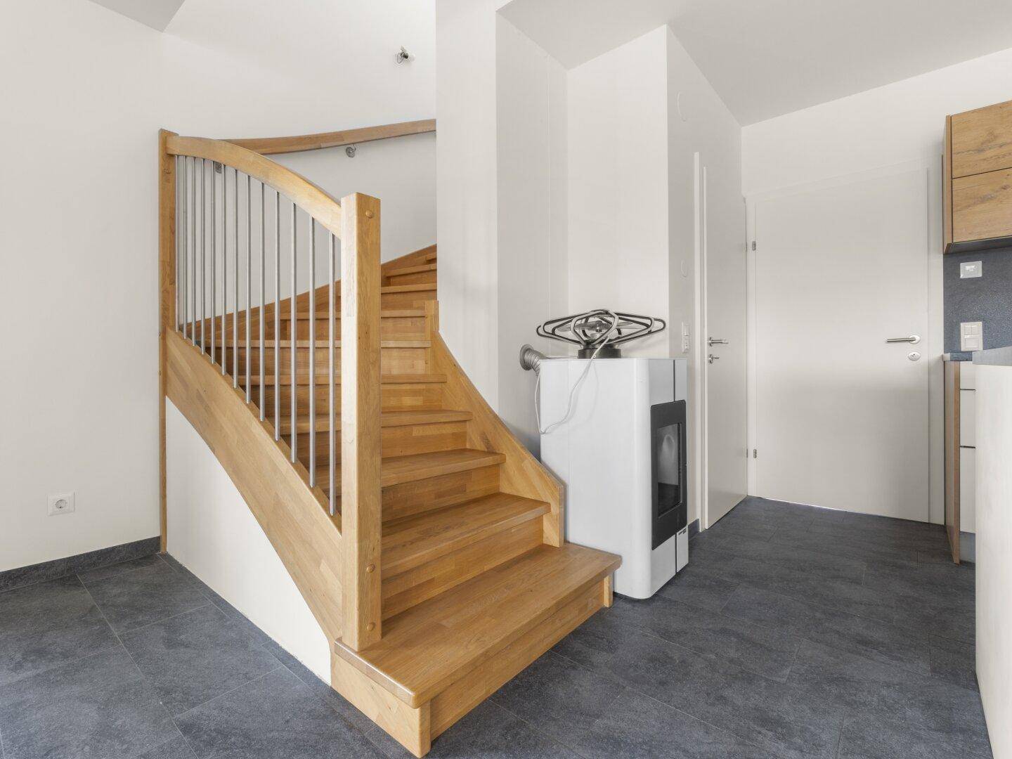 Heller Treppenaufgang aus Holz mit modernem Kaminofen im offenen Wohnbereich.