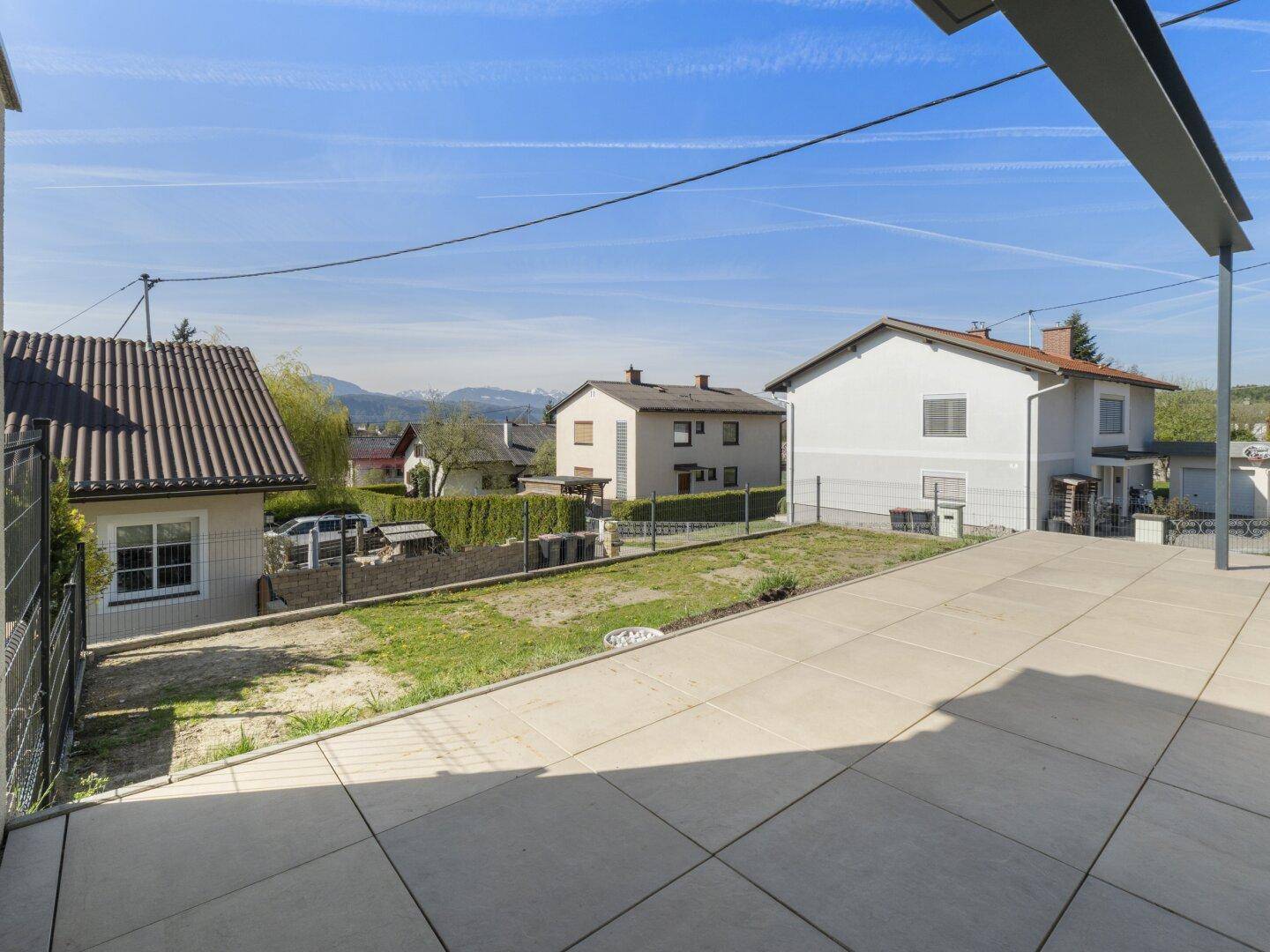 Geräumige Terrasse mit Fliesenboden und Blick auf die umliegende Wohngegend und Berge.