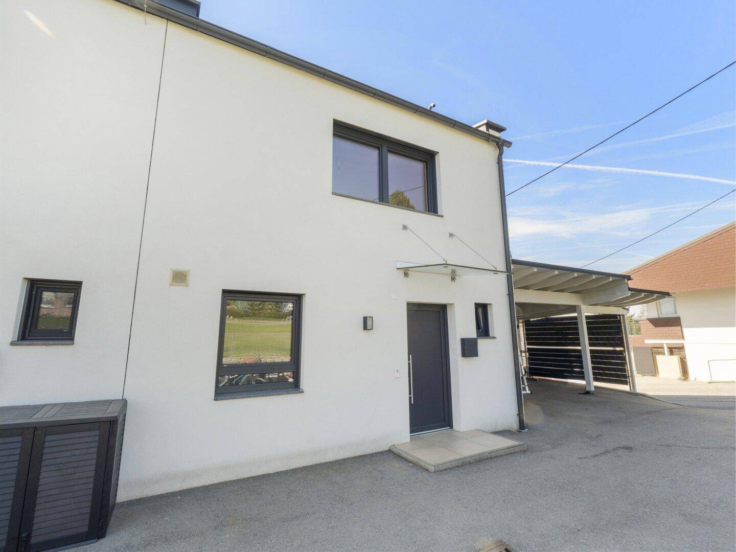 Moderner Hauseingang mit dunkler Tür und Vordach, daneben ein Carportbereich.