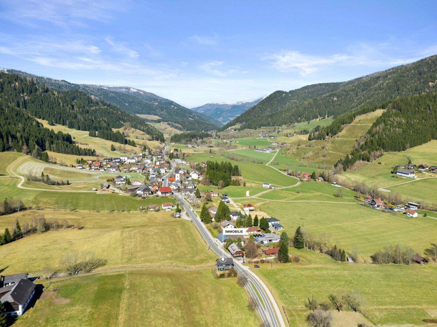 Panoramablick auf ein idyllisches Dorf in einem Tal mit markierter Immobilienlage.