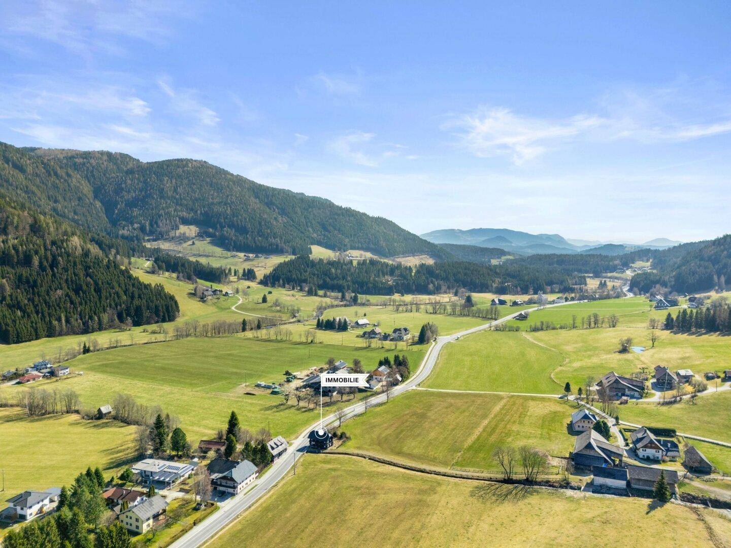 Weitwinkelaufnahme der Immobilie in einer weiten, grünen Landschaft mit Bergen im Hintergrund.
