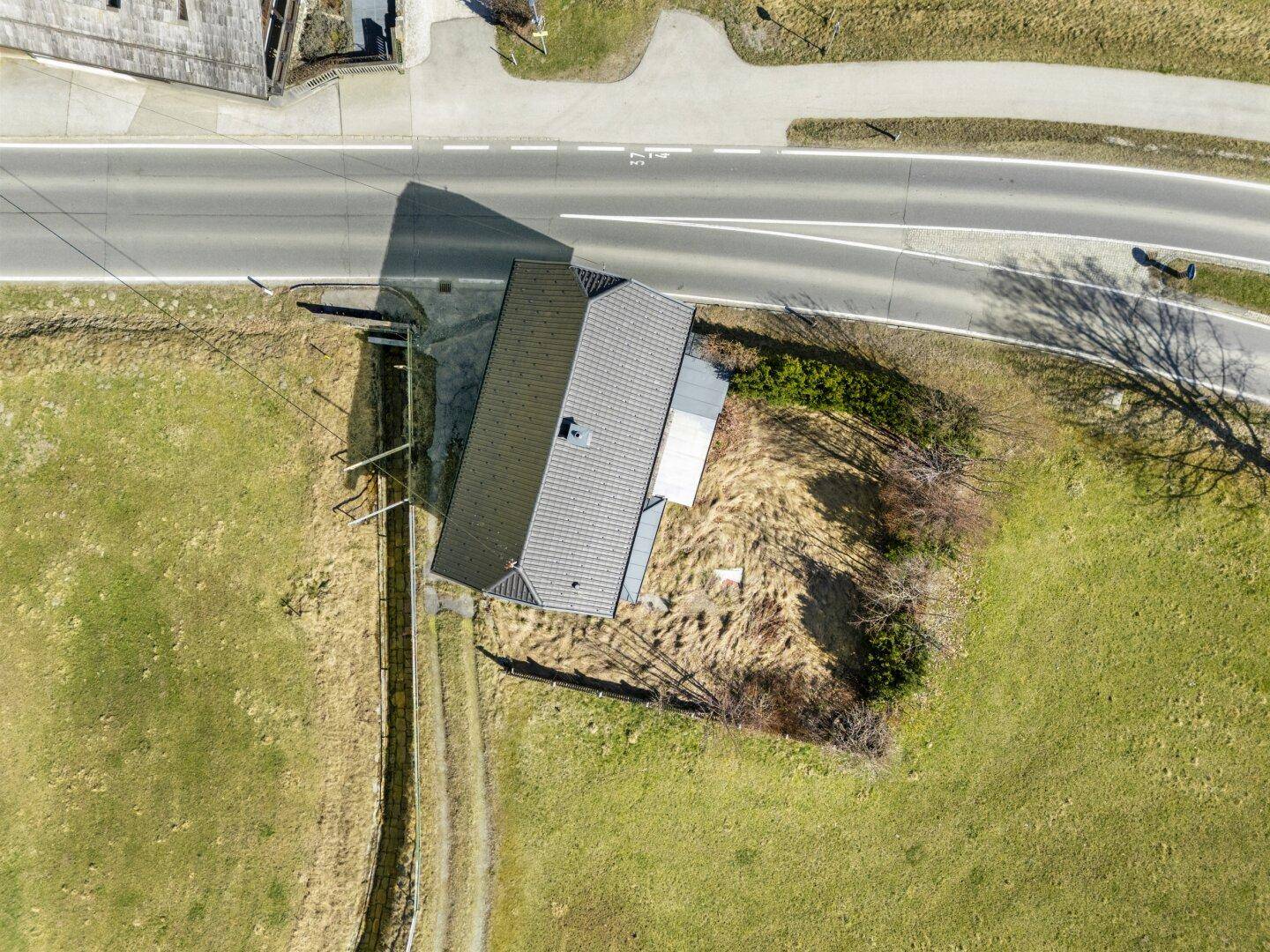 Luftaufnahme des Hauses mit Satteldach und angrenzender Straße, umgeben von grünen Feldern.