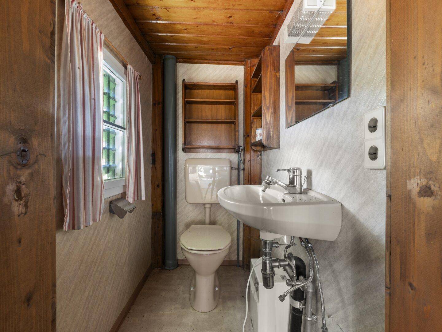 Kleines WC mit Waschbecken, Toilette und Holzvertäfelung, mit Fenster.
