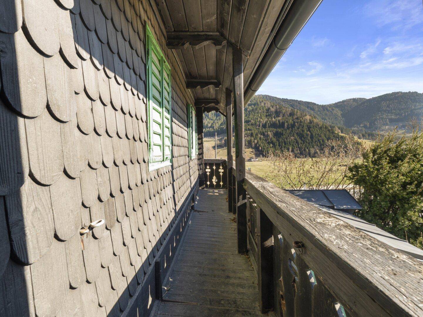 Langer Holzbalkon mit traditionellem Geländer und weitem Blick auf die Landschaft.