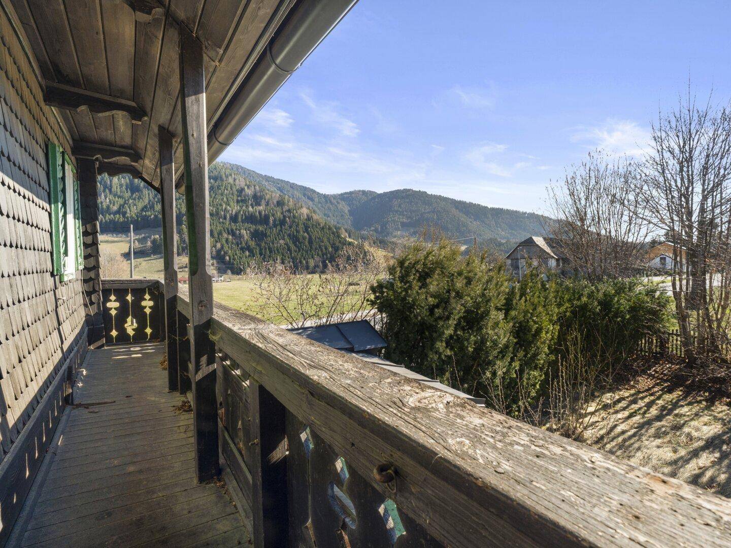 Traditioneller Holzbalkon mit Blick auf die grüne Umgebung und bewaldete Hügel.