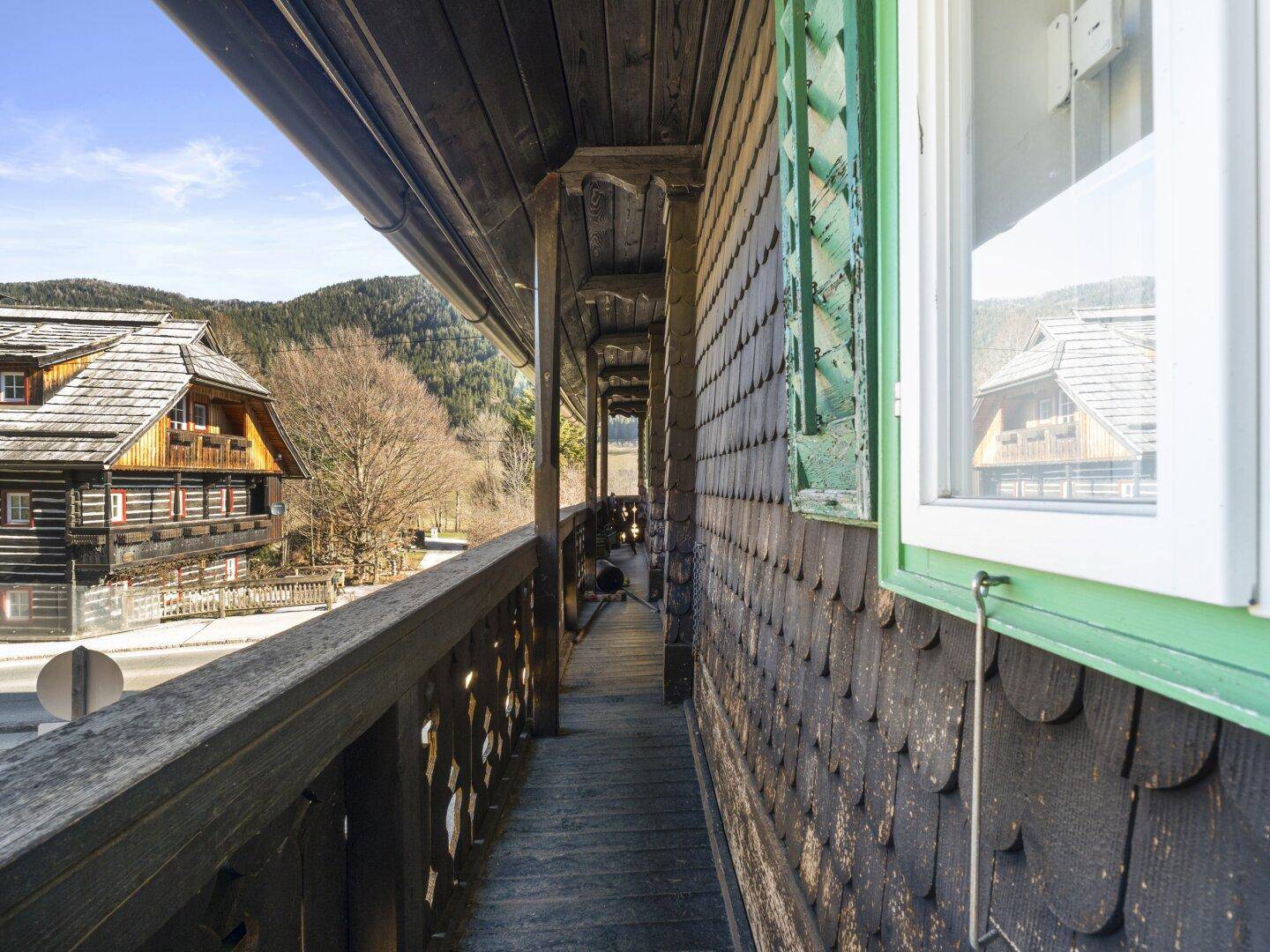 Schmaler Holzbalkon entlang der Hausfassade mit Blick auf benachbarte Gebäude.