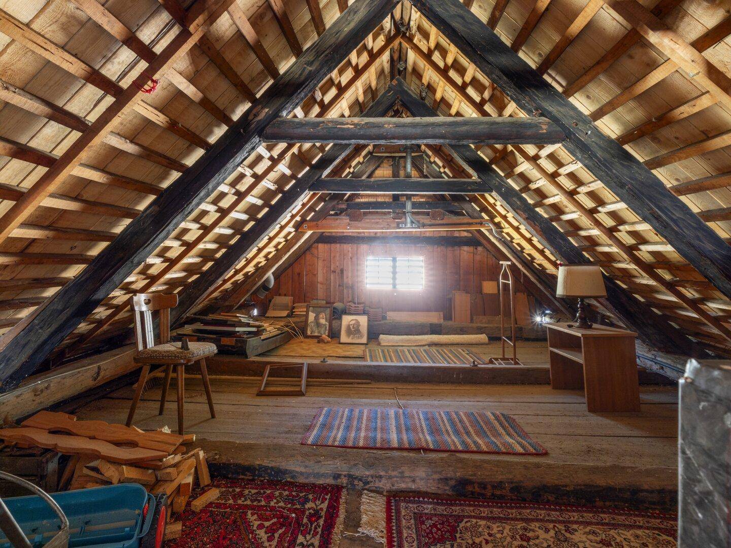 Geräumiger Dachboden mit sichtbaren Holzbalken, Holzboden und einem Fenster.