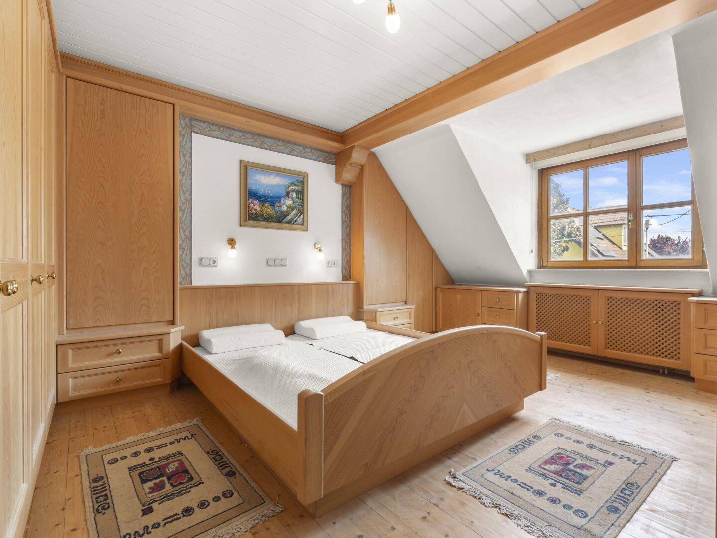 Helles Schlafzimmer mit Holzbett, Einbauschränken und schrägen Decken im Dachgeschoss.