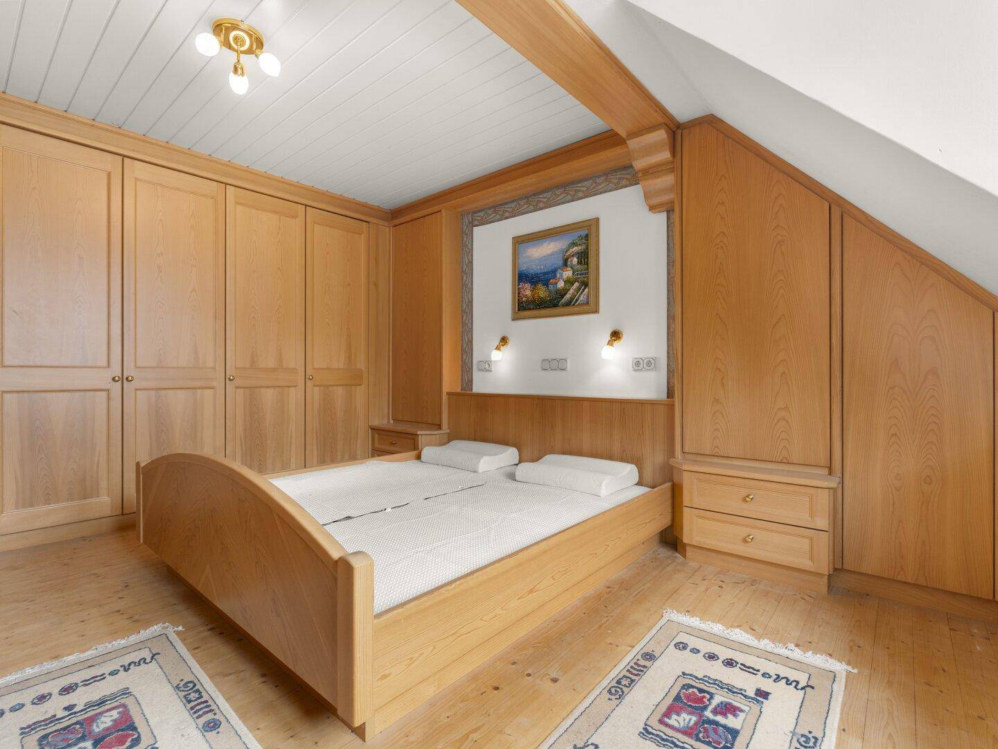 Gemütliches Schlafzimmer mit Holzbett, maßgefertigten Schränken und Holzbalken an der Decke.
