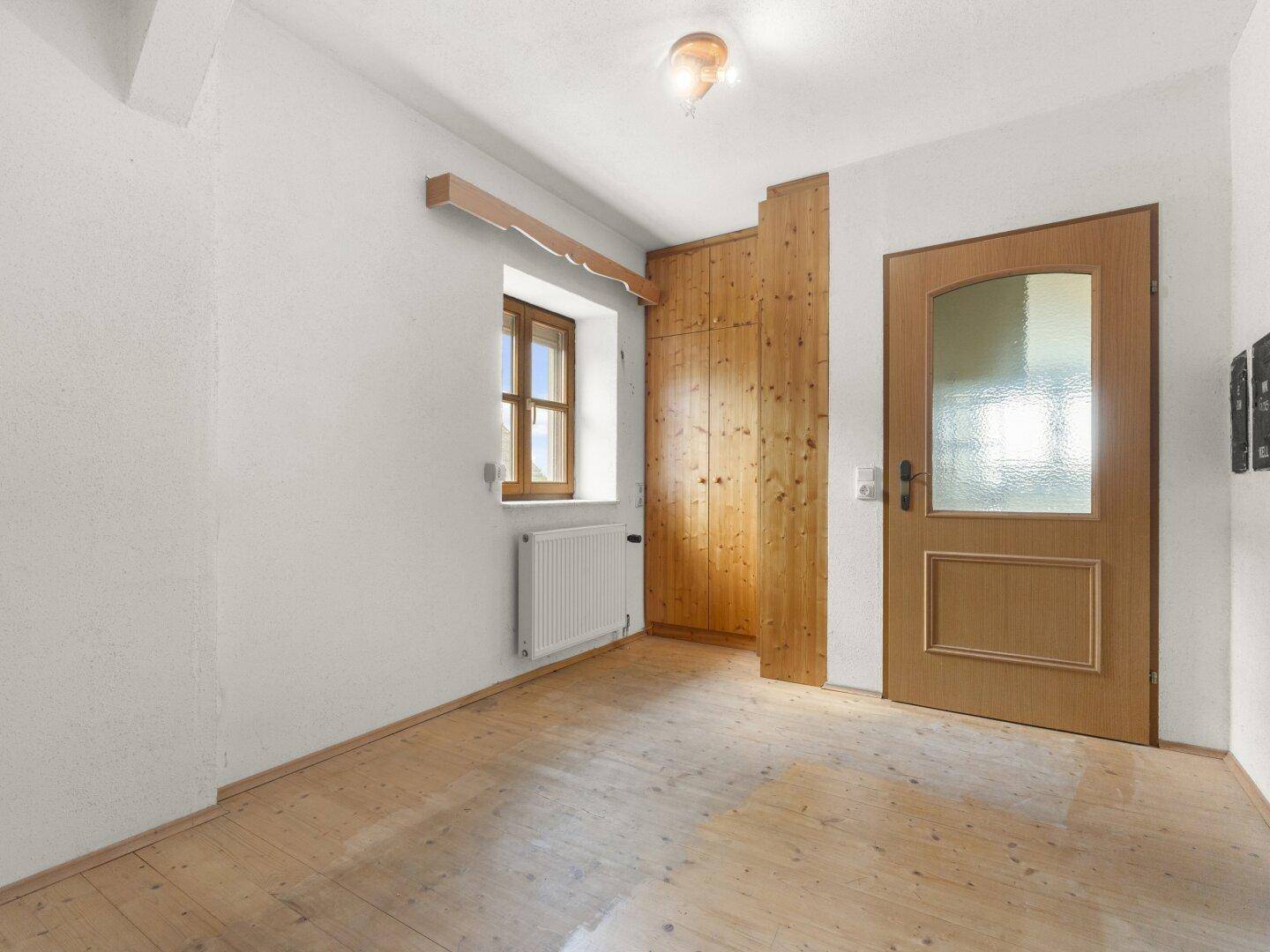 Kleiner Raum mit Holzboden, Fenster und Heizkörper, ideal als Büro oder Gästezimmer.