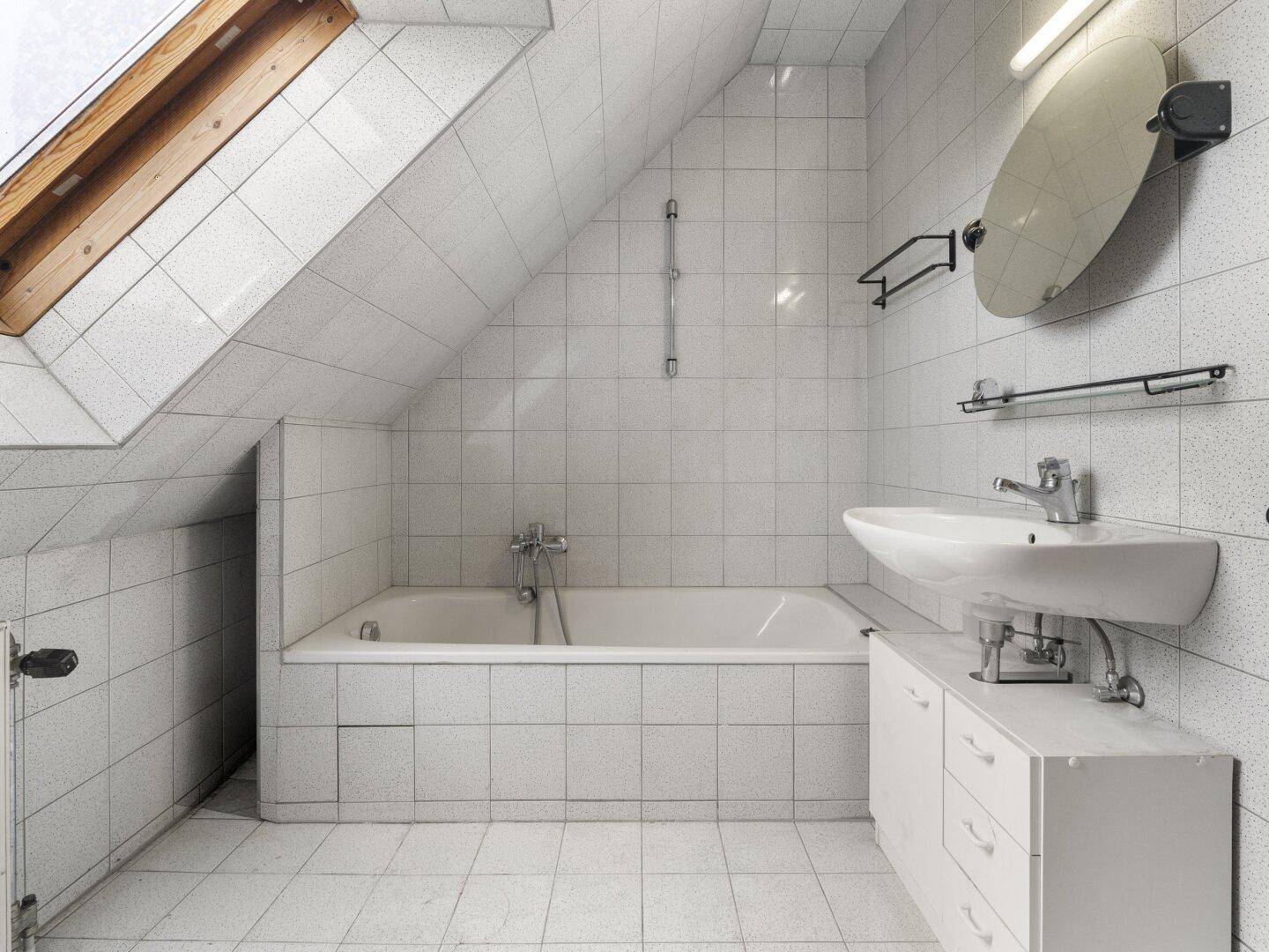 Badezimmer im Dachgeschoss mit Badewanne, Waschbecken und Dachfenster für natürliches Licht.