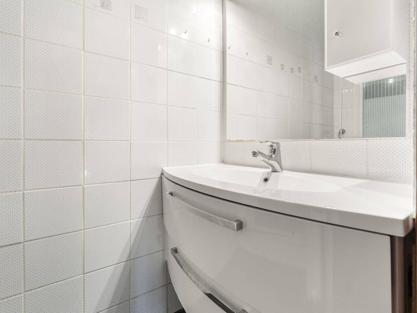 Modernes Waschbecken mit Spiegelschrank und weißen Fliesen in einem kleinen Bad.