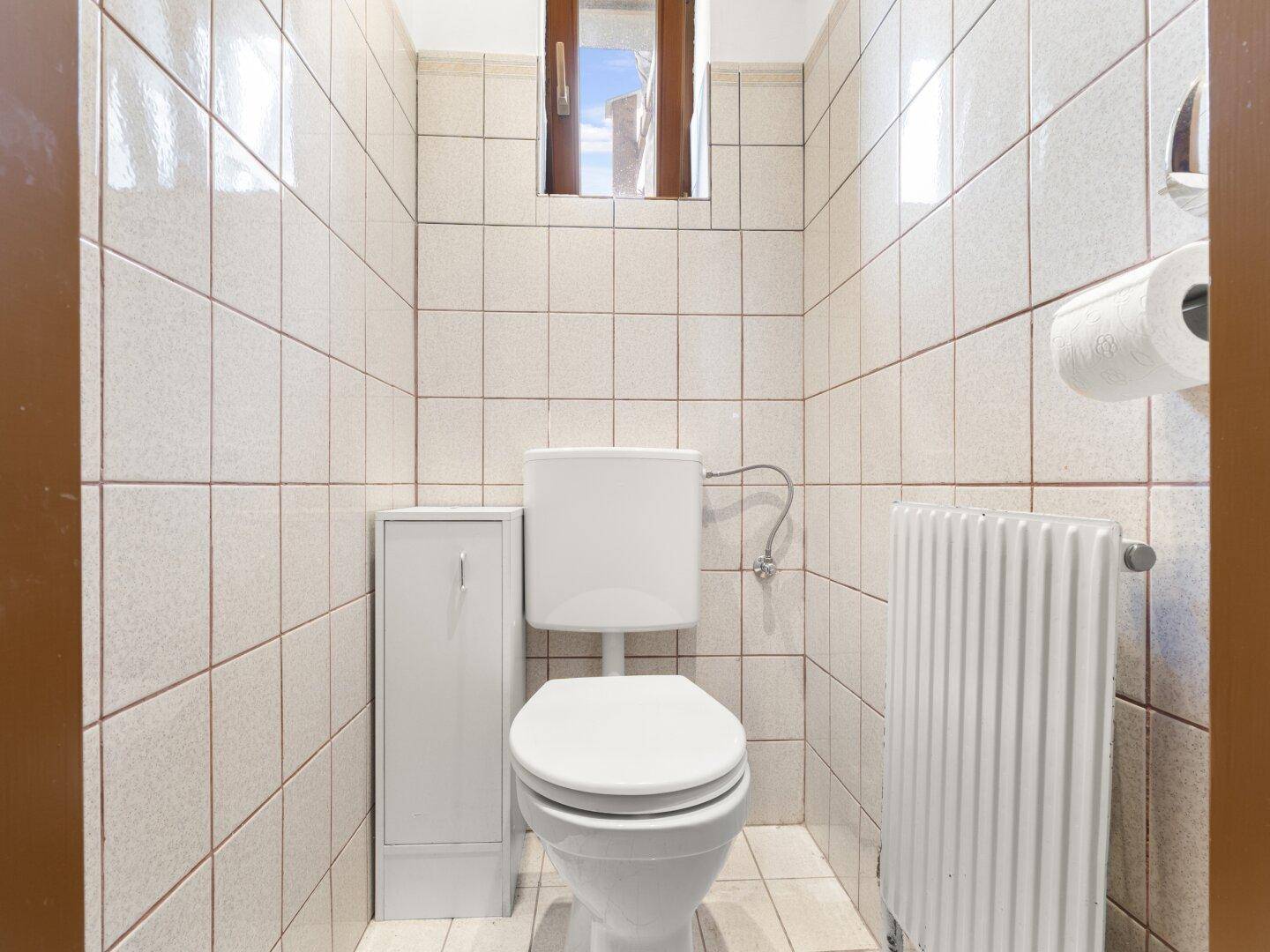 Separates WC mit Fenster, Toilette und Heizkörper, komplett gefliest in hellem Design.
