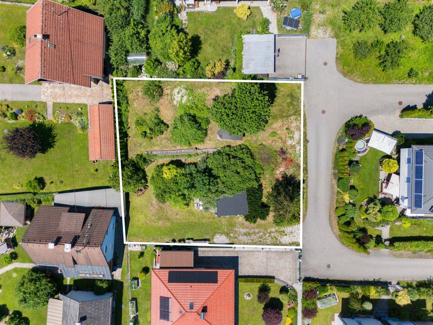 Draufsicht auf ein umrandetes Grundstück mit Bäumen und Rasen, umgeben von Wohnhäusern.