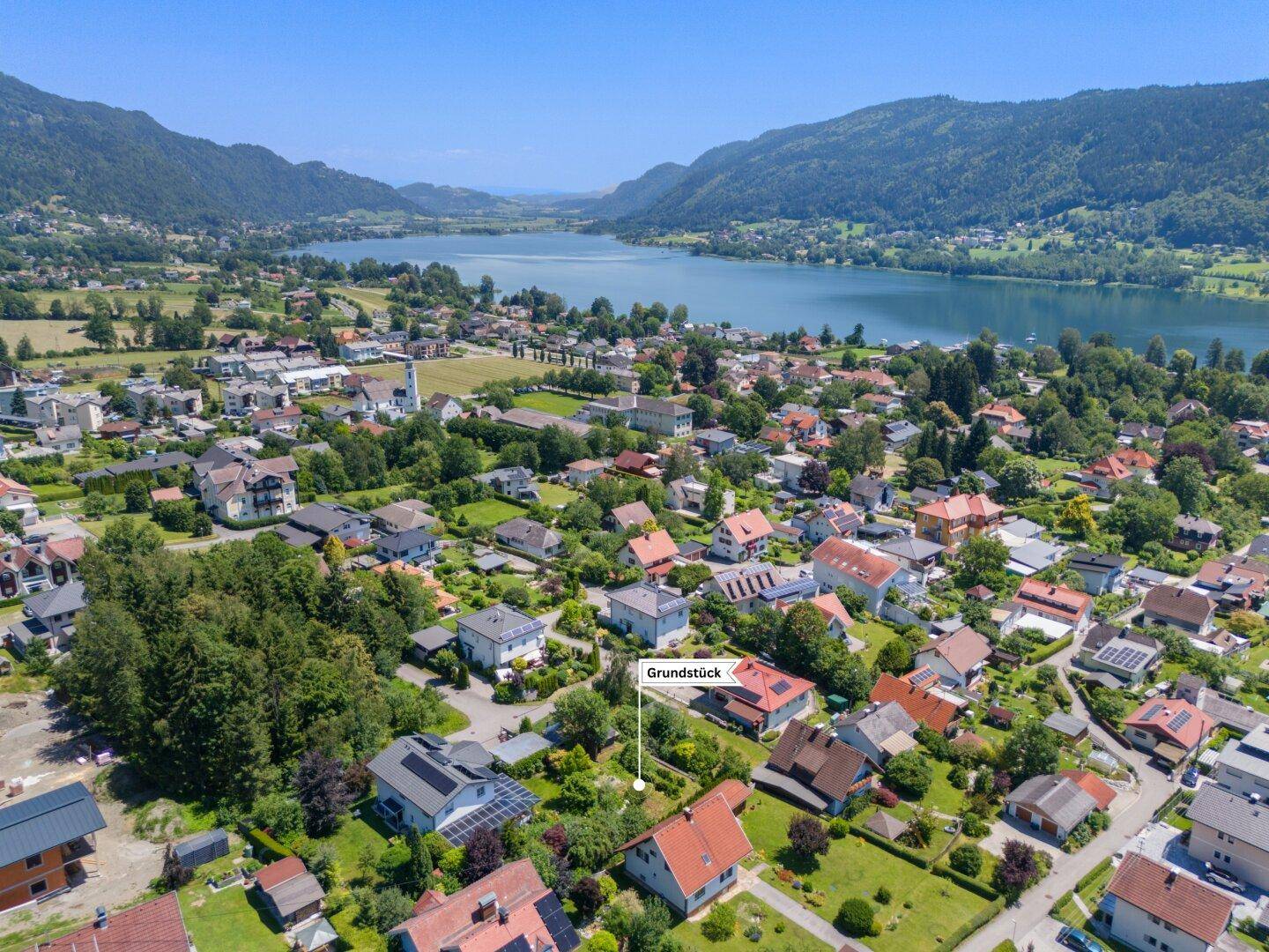 Weitläufige Luftaufnahme einer Wohnsiedlung mit See- und Bergblick, das Grundstück ist hervorgehoben.