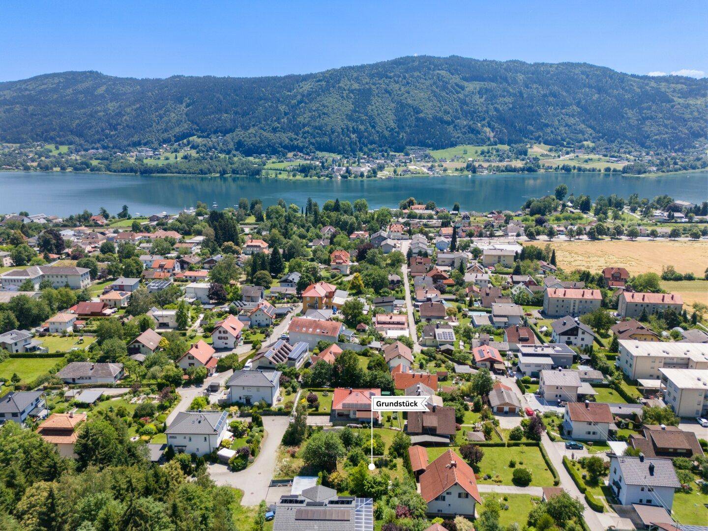 Luftaufnahme einer Siedlung am Seeufer mit Bergen im Hintergrund, das Grundstück ist markiert.