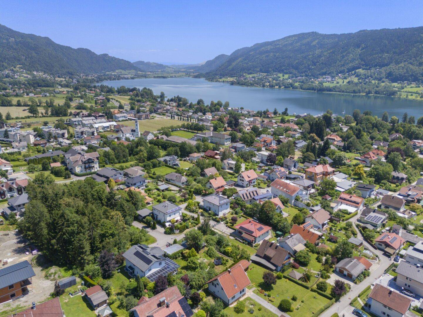 Weitläufige Luftaufnahme einer Wohnsiedlung mit See- und Bergblick, das Grundstück ist hervorgehoben.