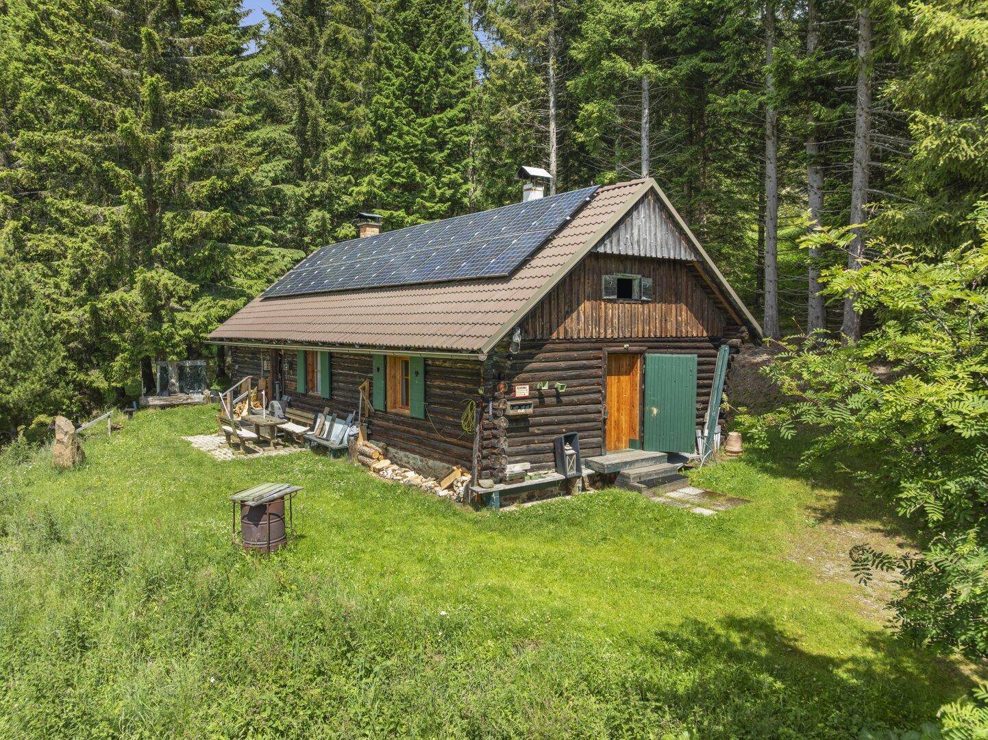 Rustikale Holzhütte mit Solaranlage auf dem Dach und grünen Fensterläden, umgeben von Natur.