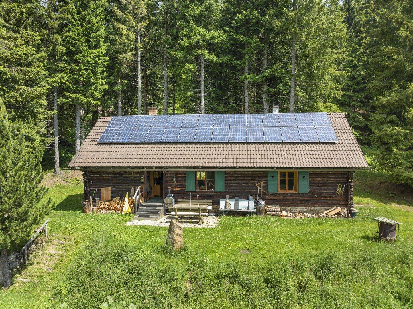 Traditionelle Holzhütte mit umfangreicher Solaranlage auf dem Dach und Sitzgelegenheiten im Freien.