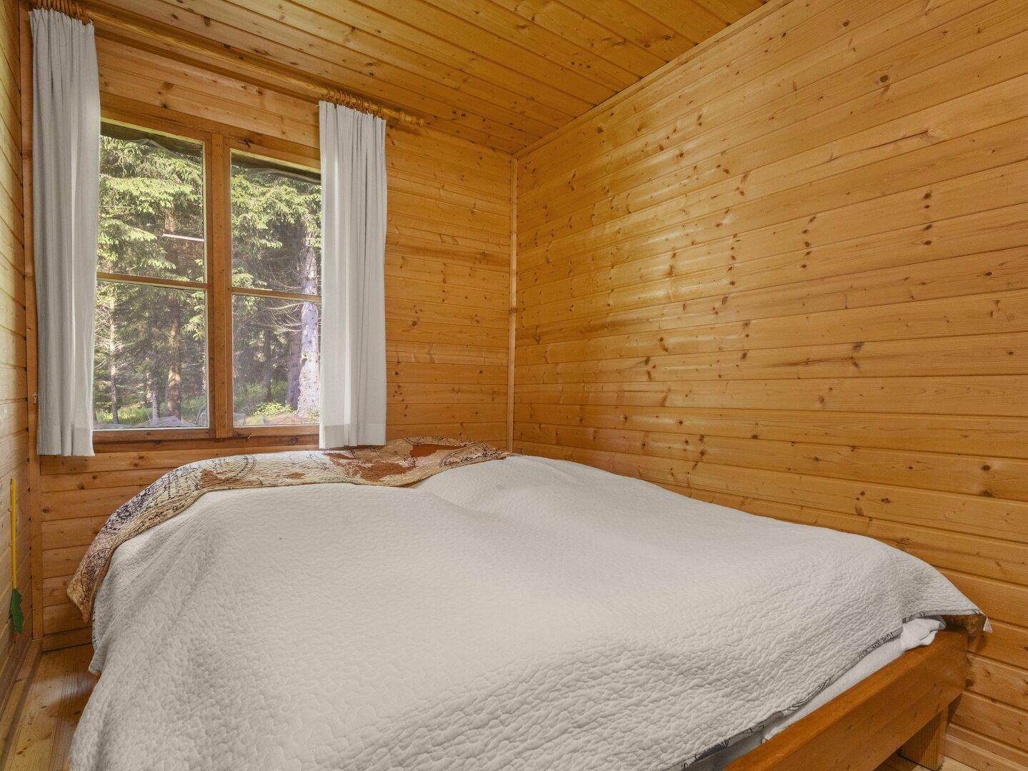 Einfaches Schlafzimmer mit Holzwänden und einem Bett, Blick auf den Wald durch das Fenster.