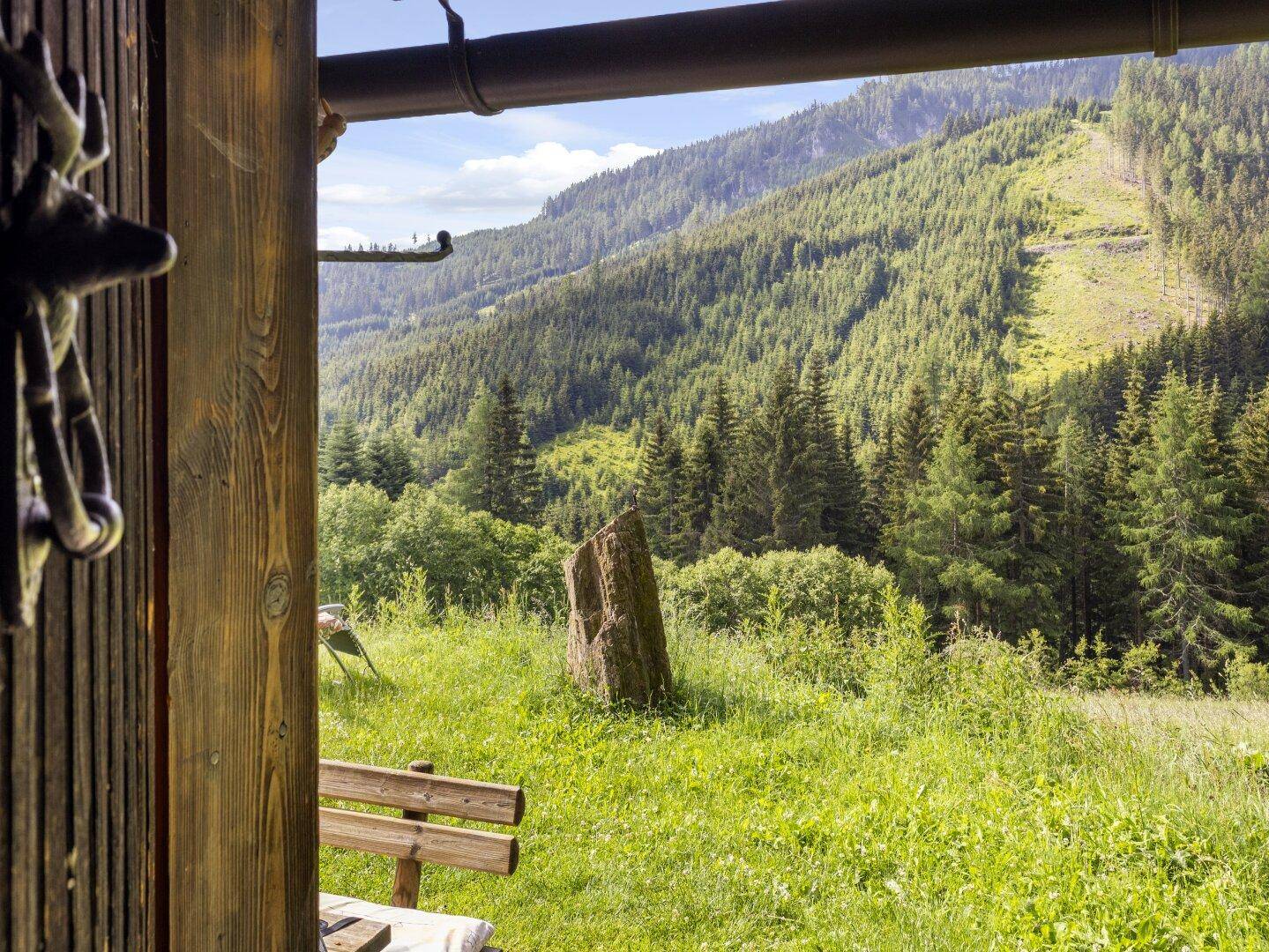 Malerischer Ausblick von einer Holzveranda auf die umliegenden grünen Berge und Wälder.