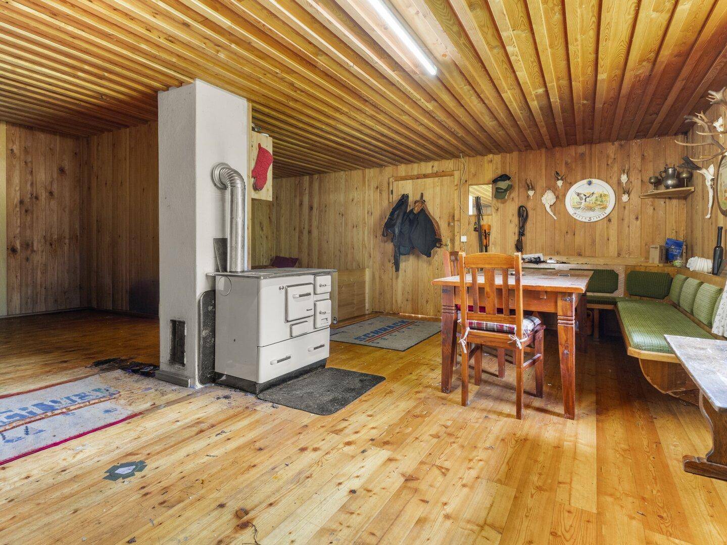 Rustikaler Wohnbereich mit Holzofen, Holzbänken und Esstisch, ideal für gesellige Runden.