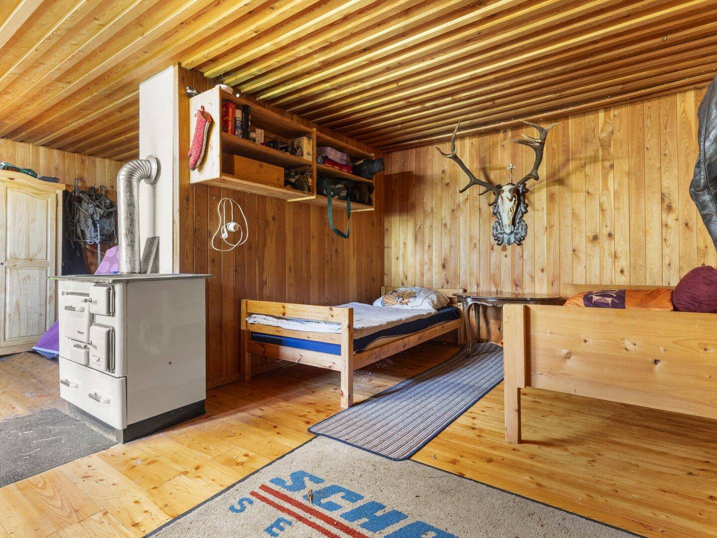 Gemütliches Schlafzimmer mit zwei Einzelbetten, Holzwänden und einem traditionellen Holzofen.