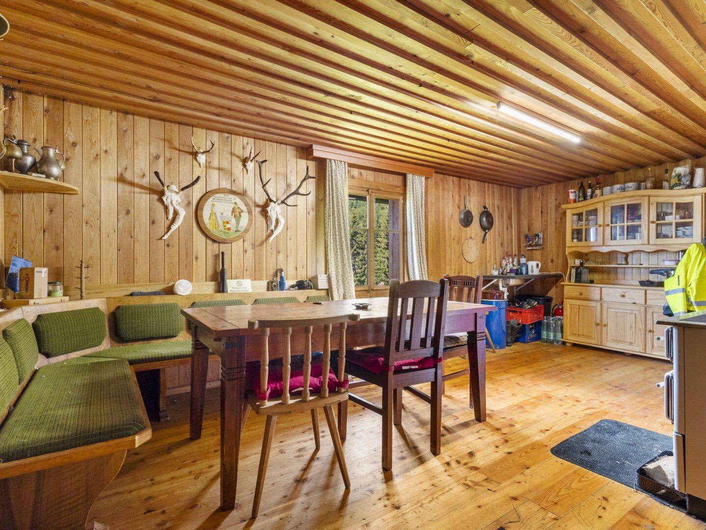Traditioneller Wohn- und Essbereich mit Holzbänken, Esstisch und Jagdtrophäen an den Wänden.