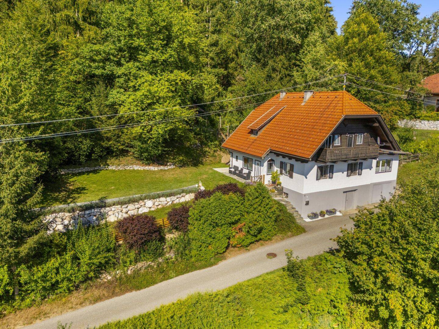 Hausansicht mit rotem Ziegeldach und großem Gartenbereich in ländlicher Umgebung.