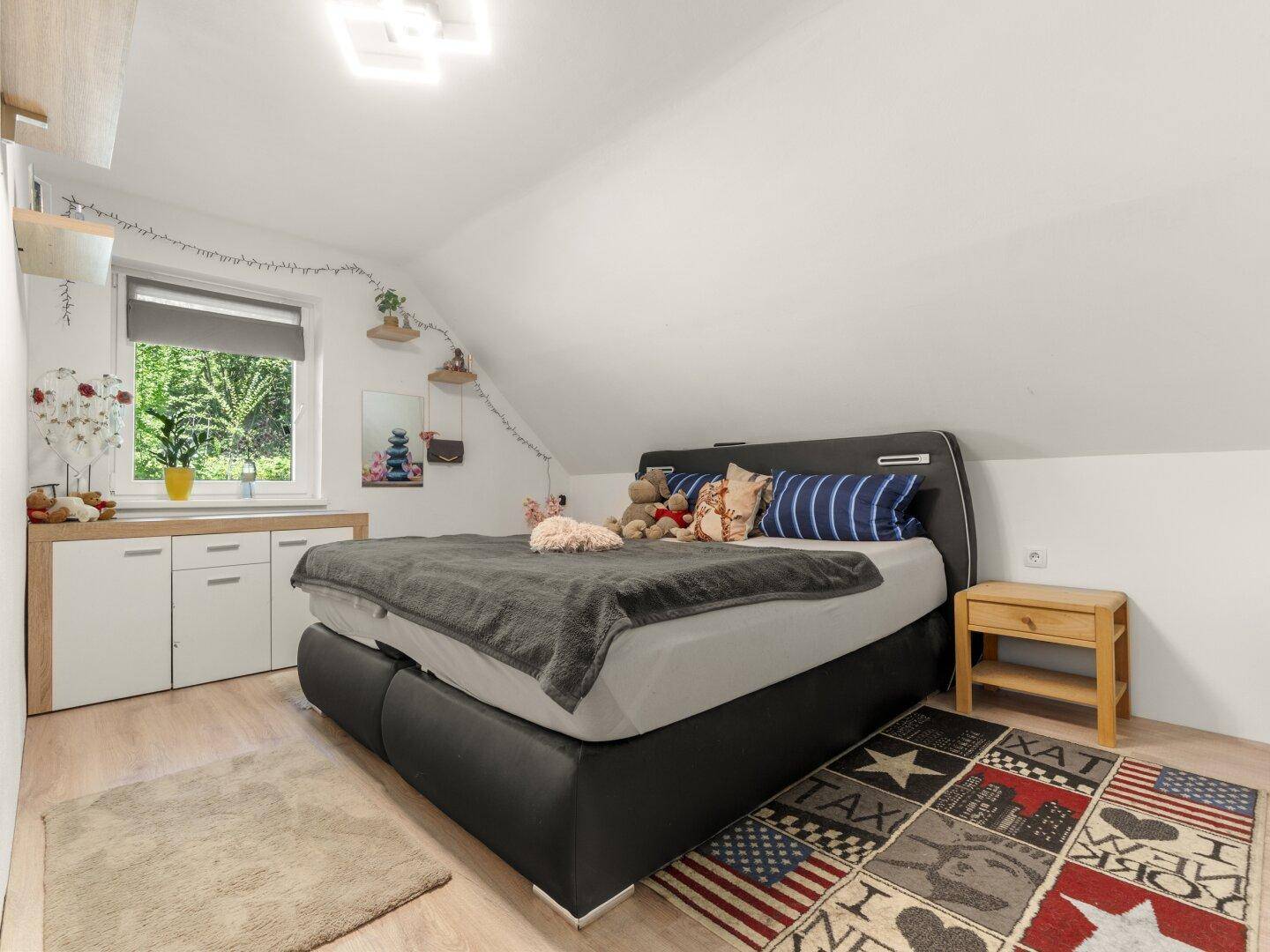 Helles Schlafzimmer mit Dachschräge, Doppelbett und Fenster mit Blick ins Grüne.