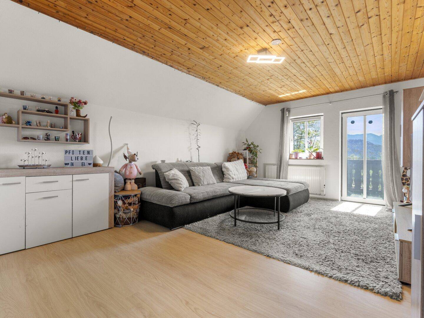 Gemütliches Wohnzimmer mit Holzbalkendecke, Sofa und Zugang zum Balkon mit Bergblick.