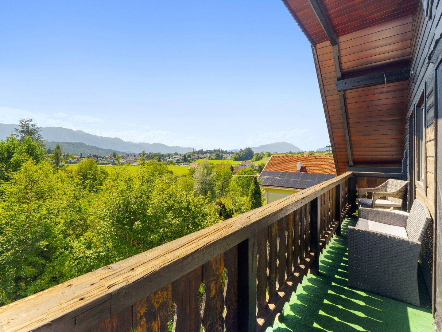 Geräumiger Holzbalkon mit Sitzgelegenheiten und weitem Blick über die Landschaft und Berge.