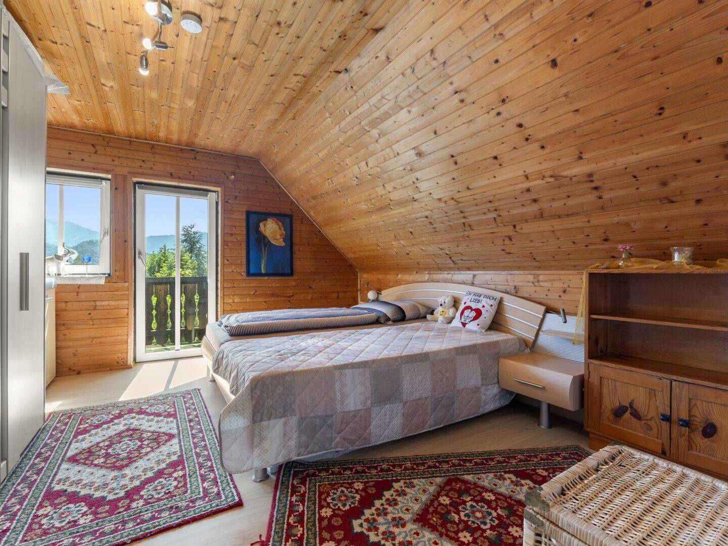 Rustikales Schlafzimmer mit Holzvertäfelung, Doppelbett und Balkonzugang mit Bergblick.