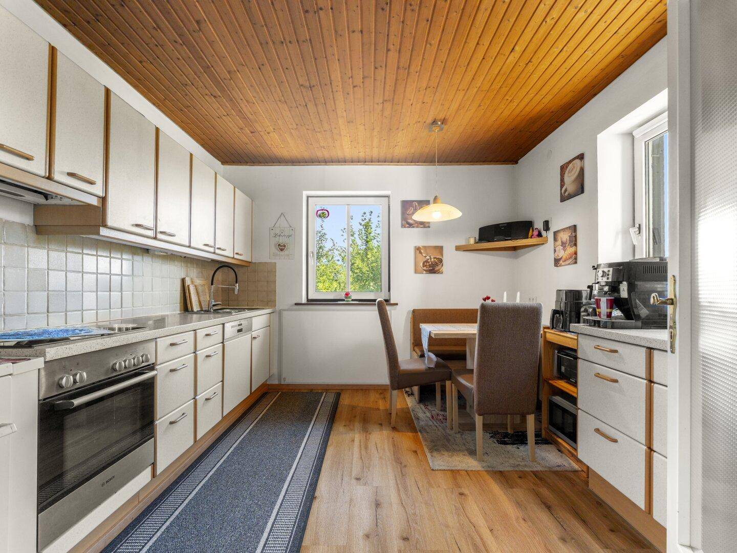 Funktionale Wohnküche mit Holzbalkendecke, Essbereich und Fenster mit Blick ins Grüne.