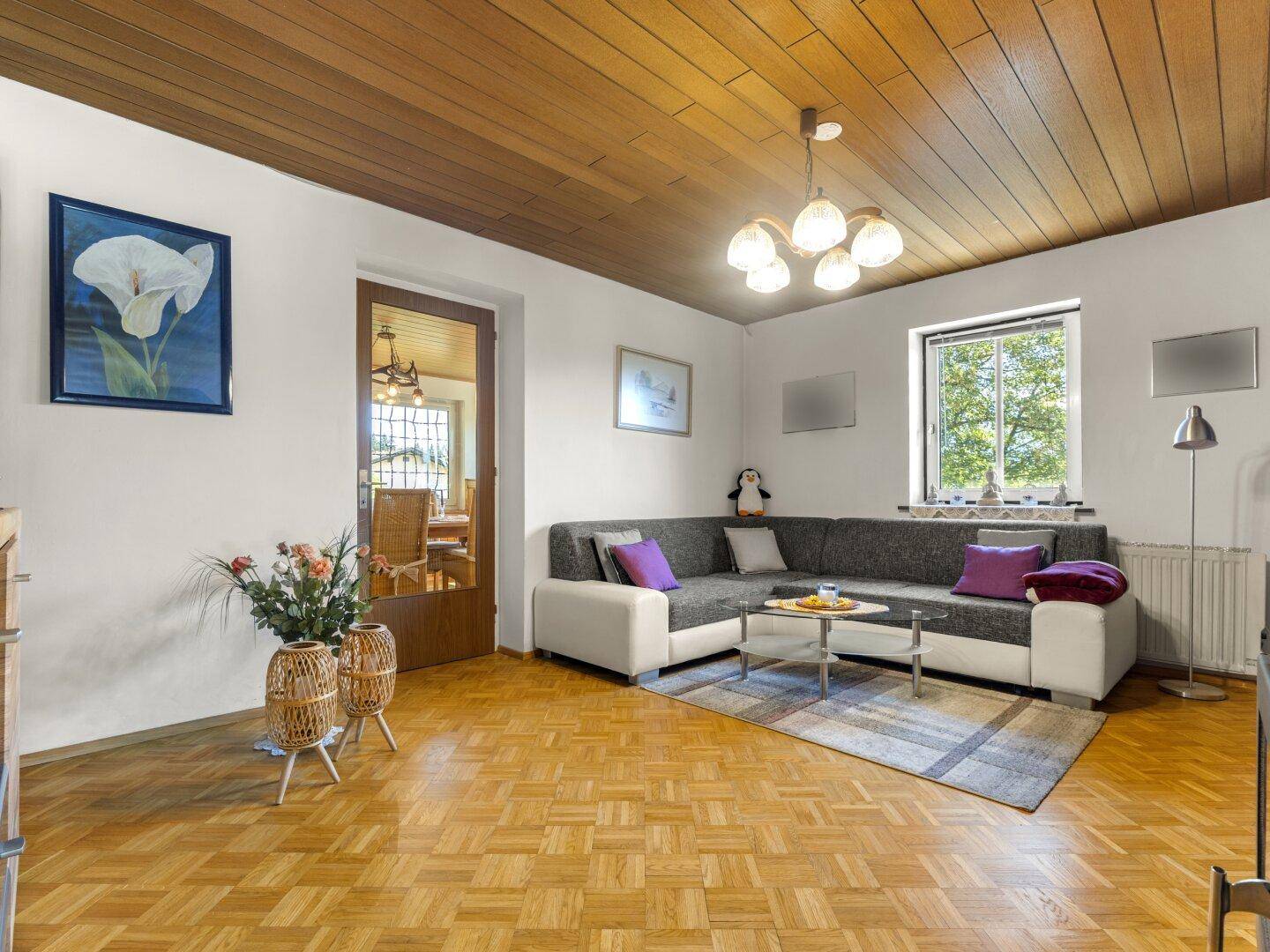 Geräumiges Wohnzimmer mit Parkettboden, Holzbalkendecke und gemütlicher Sitzecke.