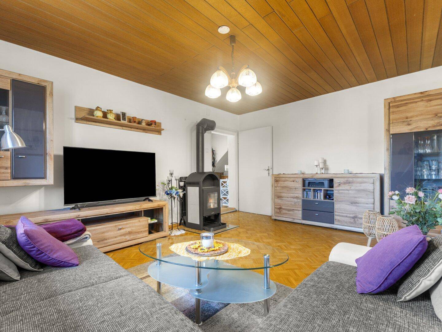 Wohnzimmer mit Kaminofen, Parkettboden und Holzdecke, ideal für gemütliche Abende.