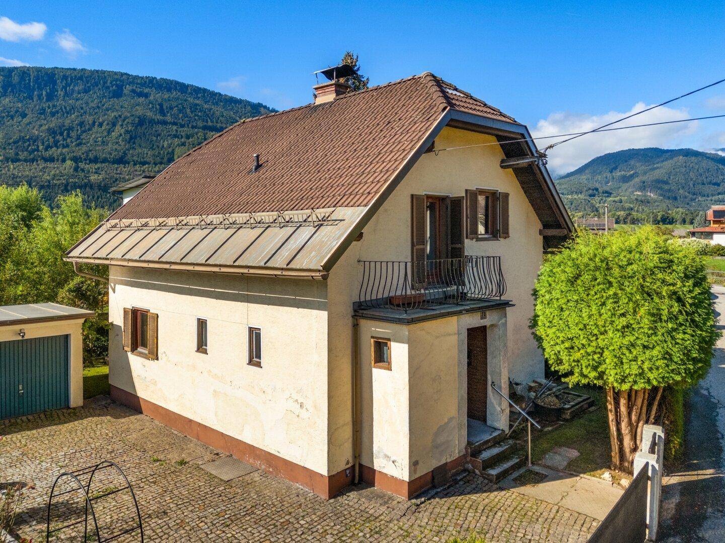 Ansicht des Einfamilienhauses mit Satteldach, kleinem Balkon und gepflastertem Vorplatz.