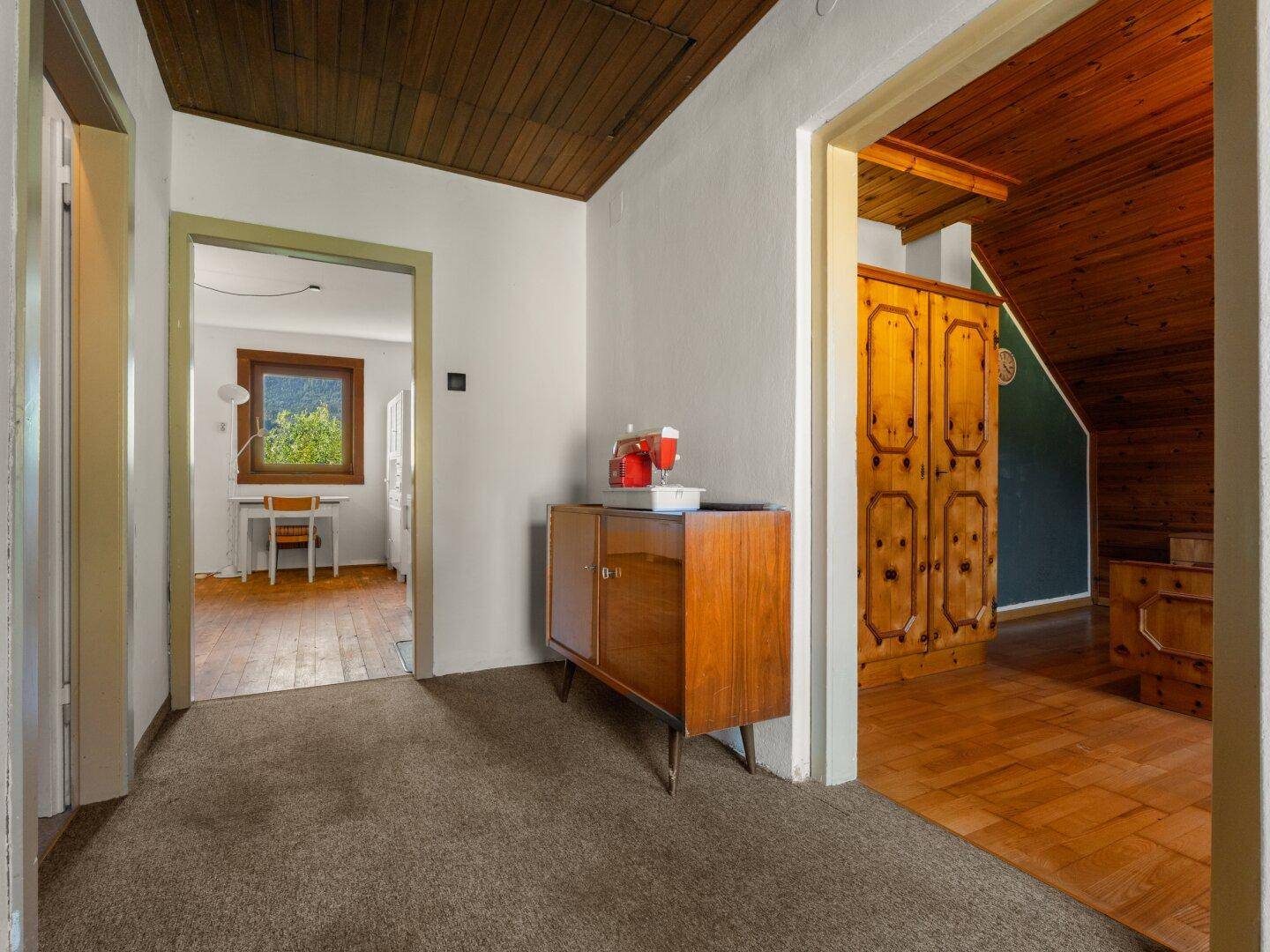 Flur mit Teppichboden, Holzdecke und einem Vintage-Schrank, der zu weiteren Räumen führt.