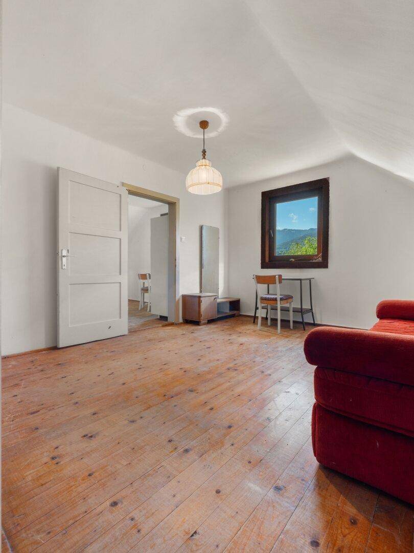 Helles Dachzimmer mit Holzdielenboden, schräger Decke und einem roten Sofa.
