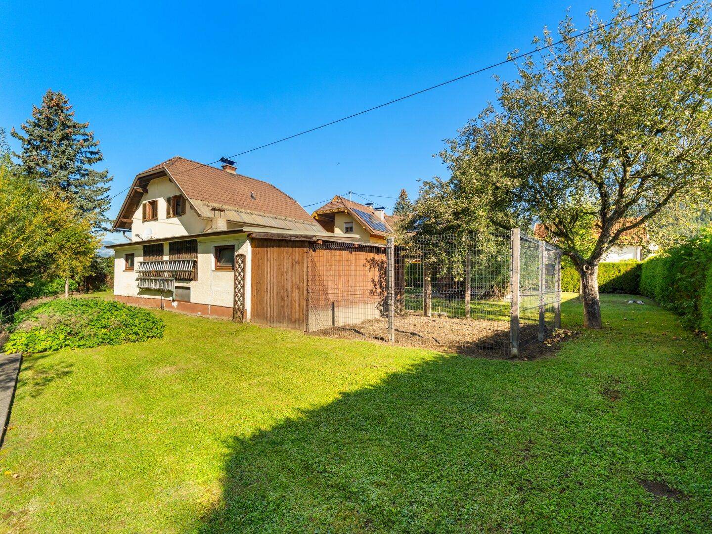 Rückansicht des Hauses mit großem Garten, Rasenfläche und Obstbaum unter blauem Himmel.